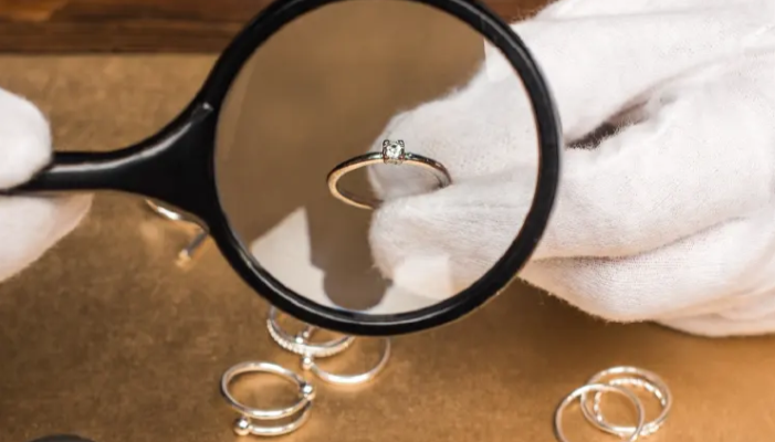 Gloved hands examining a ring with a magnifier.